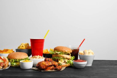 French fries, burgers and other fast food on wooden table against white background