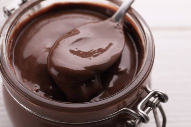 Lezzetli çikolata ezmeli kavanoz ve beyaz ahşap masada kaşık, yakın plan.