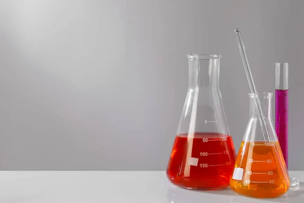 灰色の背景に白いテーブルの上にカラフルな液体を持つ異なる研究室のガラス製品 テキストのスペース — ストック写真