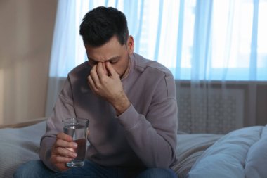 Yatak odasında bir bardak suyla üzgün bir adam. Yalnızlık kavramı