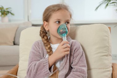 Evdeki koltukta nefes almak için nebulizör kullanan küçük kız.