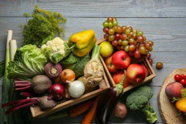 Different fresh vegetables and fruits in crates on grey wooden table, flat lay. Farmer harvesting