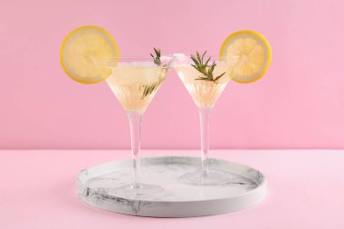 Limon dilimli martini bardakları ve pembe arka planda mermer tepside biberiye.