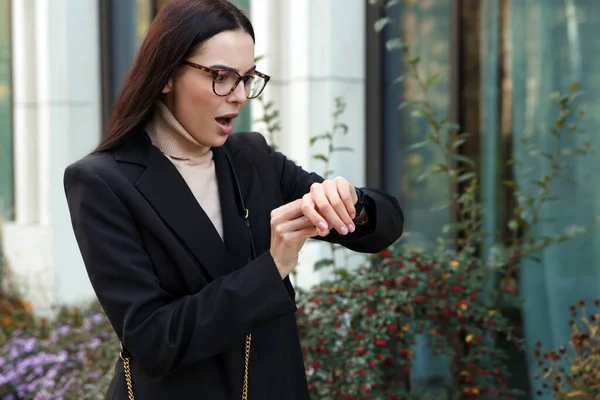 Emotional woman checking time on watch outdoors. Being late concept