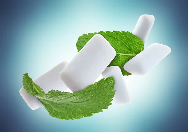 Fresh mint leaves and chewing gum pads falling on light blue background