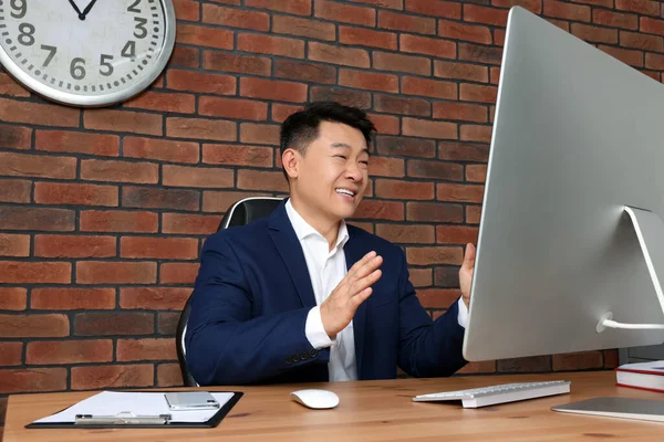 Happy boss having online meeting via computer at wooden table in modern office