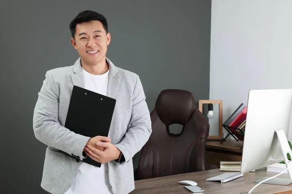 Happy boss holding clipboard in his modern office