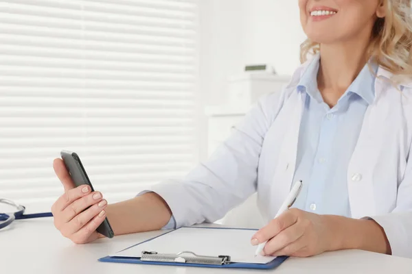 病院のデスクでスマートフォンとクリップボードを持つ医師 クローズアップ オンライン医学の概念 — ストック写真