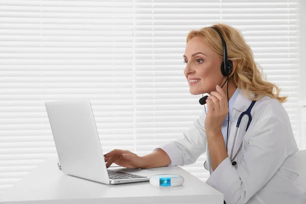 Doctor with laptop and headphones consulting patient in clinic. Online medicine concept