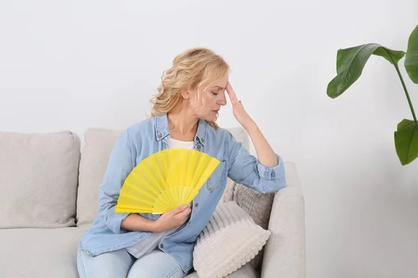 Woman waving hand fan to cool herself at home. Hormonal disorders