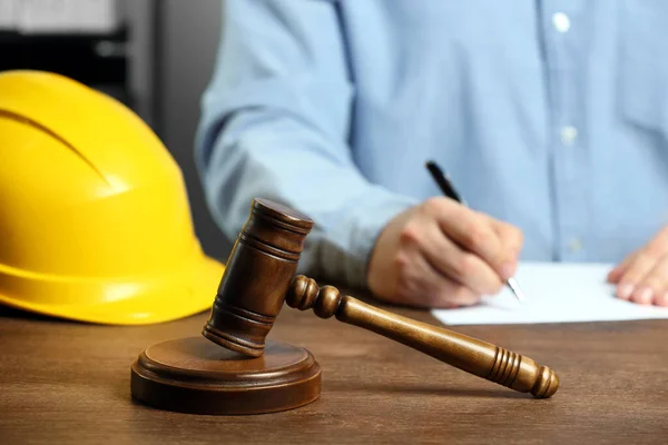 Construction and land law concepts. Man writing at wooden table, focus on gavel