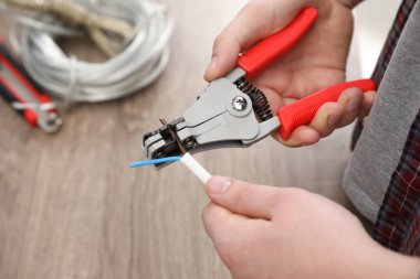Professional electrician stripping wiring at wooden table, above view