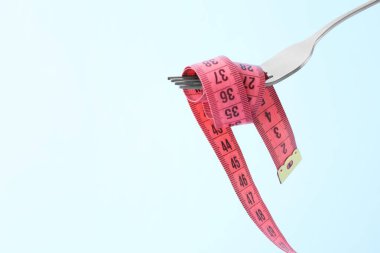 Fork with measuring tape on light blue background, space for text. Diet concept