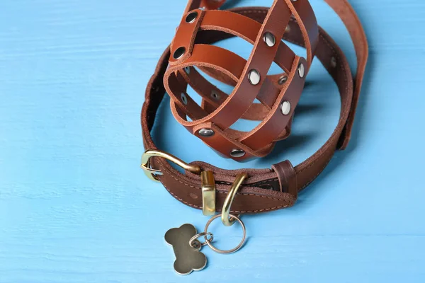 Brown leather dog muzzle and collar on light blue wooden table