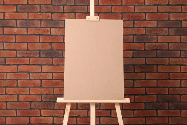stock image Wooden easel with blank board near brick wall