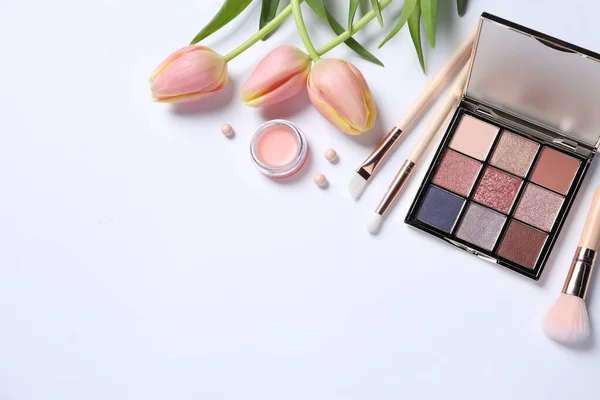 Flat lay composition with makeup products and beautiful tulips on white background. Space for text