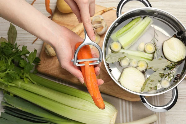 stock image Cooking tasty bouillon. Woman peeling carrot at white wooden table, top view