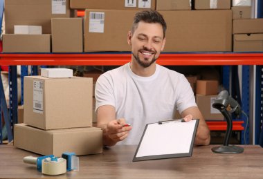 Post office worker with clipboard and parcels at counter indoors