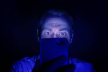 İnternet bağımlılığı. Geceleri akıllı telefon kullanan bir adam. Maviyle kaplanmış.