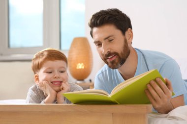 Father reading book with his child on bed at home