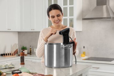 Woman using thermal immersion circulator at table in kitchen. Sous vide cooking clipart