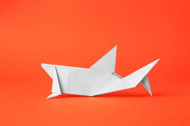 Origami sanatı. Turuncu arka planda el yapımı beyaz kağıt köpekbalığı.