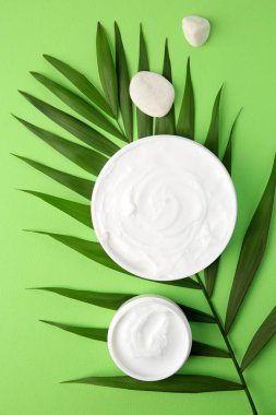 Jars of cream, leaf and stones on light green background, flat lay
