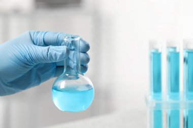 Laboratuvarda açık mavi sıvı şişesini tutan bilim adamı, yakın plan. Metin için boşluk