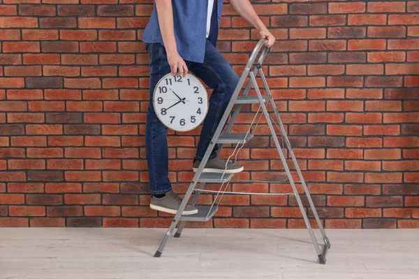 Man holding clock on stepladder near red brick wall, closeup