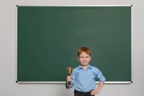 Pupil with school bell near green chalkboard in classroom