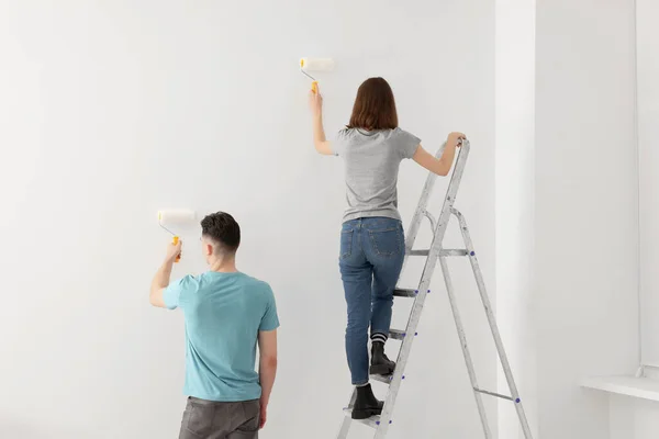 Young man and woman painting wall with rollers indoors. Room renovation
