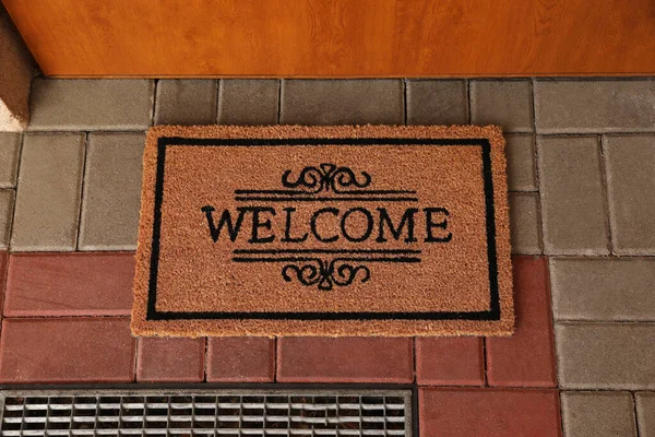Door mat with word Welcome on street tiles near entrance, top view