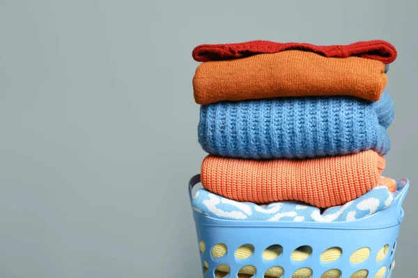 Plastic laundry basket with clean clothes on grey background. Space for text
