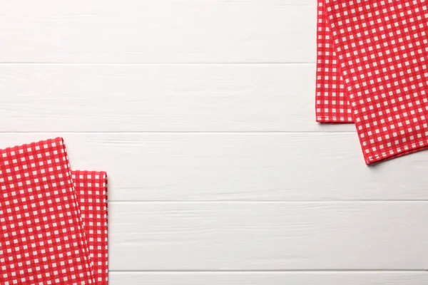 stock image Red checkered tablecloths on white wooden table, flat lay. Space for text