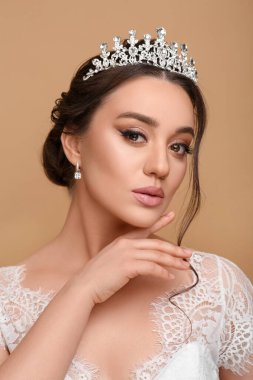 Bej arka planda lüks bir taç takan güzel bir genç kadın.