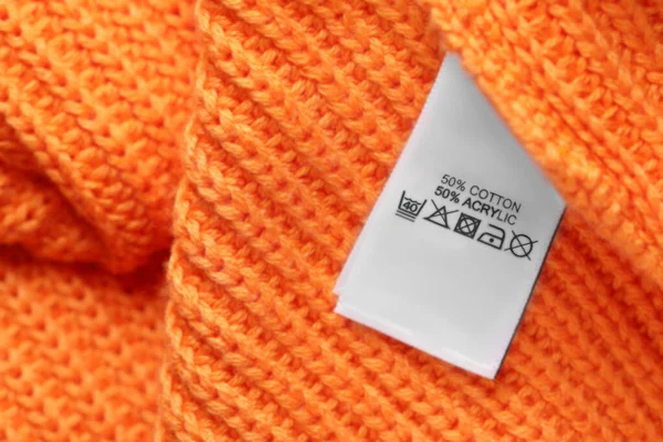 Clothing label with care recommendations on orange garment, top view. Space for text