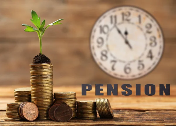 Pension plan. Stacks of coins with green sprout on wooden table and clock