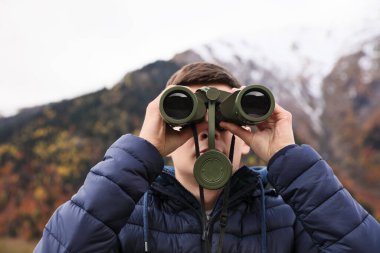 Boy looking through binoculars in beautiful mountains, closeup