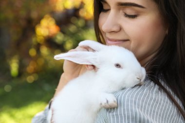 Happy woman with cute rabbit outdoors on sunny day, closeup. Space for text clipart