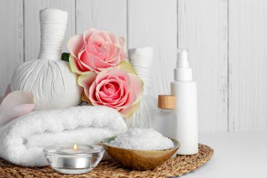 Beyaz masadaki farklı spa ürünleri, mum ve güllerle ahşap arka planda kompozisyon