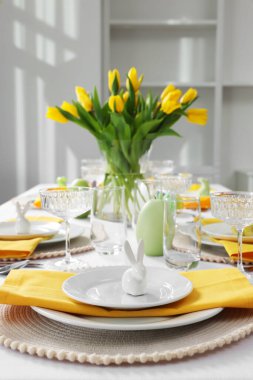 Festive table setting with glasses, painted eggs and vase of tulips. Easter celebration
