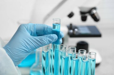 Scientist taking test tube with light blue liquid in laboratory, closeup