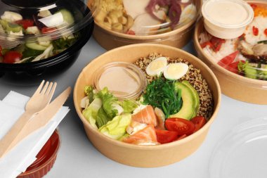 Konteynırlarda lezzetli yemekler, tahta bıçak ve çatalla açık gri masada.