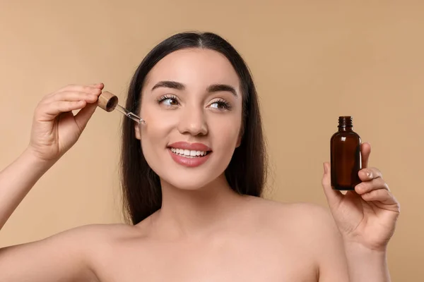 Glad Ung Kvinna Med Flaska Tillämpa Eterisk Olja Ansiktet Beige — Stockfoto