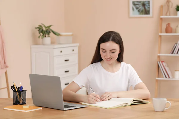 在室内木桌边的笔记本电脑上工作时 妇女在笔记本上写字 — 图库照片