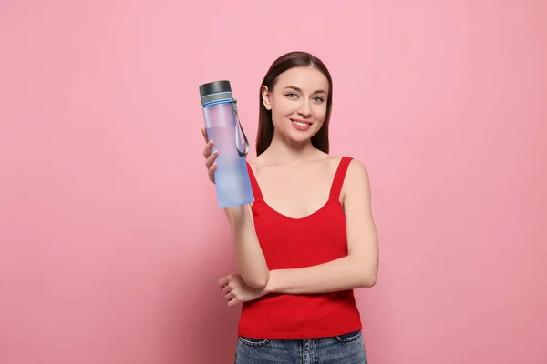 ピンクの背景に水のための透明なボトルを持つ美しい若い女性 — ストック写真