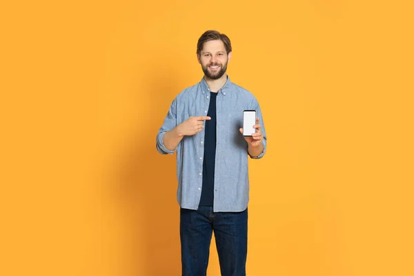 オレンジの背景にスマートフォンを示すカジュアルな服の男 — ストック写真