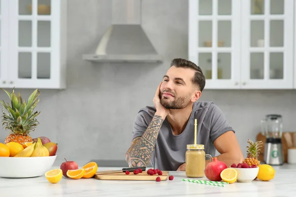 stock image Handsome man with delicious smoothie and ingredients at white table in kitchen. Space for text