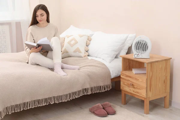 Γυναίκα Ανάγνωση Βιβλίο Κοντά Φορητό Ηλεκτρικό Θερμαντήρα Ανεμιστήρα Στο Υπνοδωμάτιο — Φωτογραφία Αρχείου
