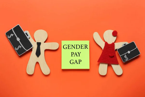 Gender pay gap. Wooden figures of man and woman, paper note on orange background, flat lay